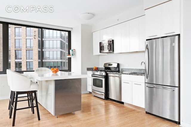 kitchen with light wood-type flooring, a kitchen bar, a sink, white cabinetry, and appliances with stainless steel finishes