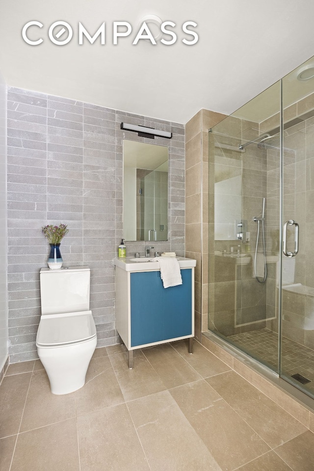 bathroom with tile walls, toilet, a stall shower, vanity, and tile patterned floors