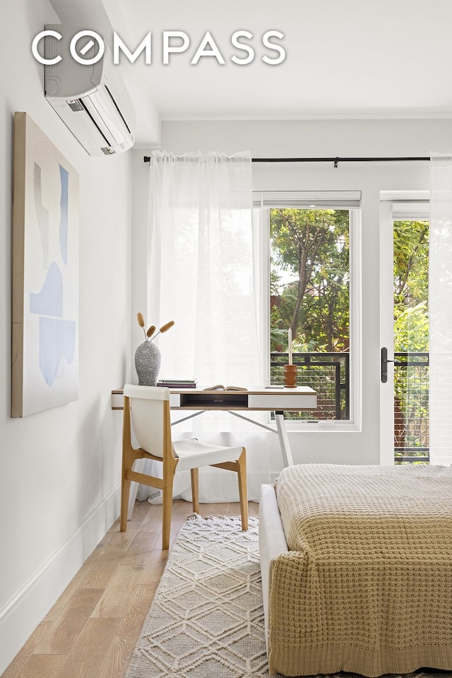 bedroom featuring a wall mounted AC, light wood-type flooring, and baseboards