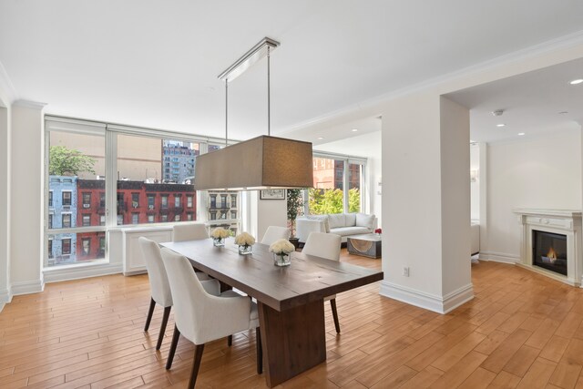 dining room with a glass covered fireplace, crown molding, light wood-style flooring, and baseboards