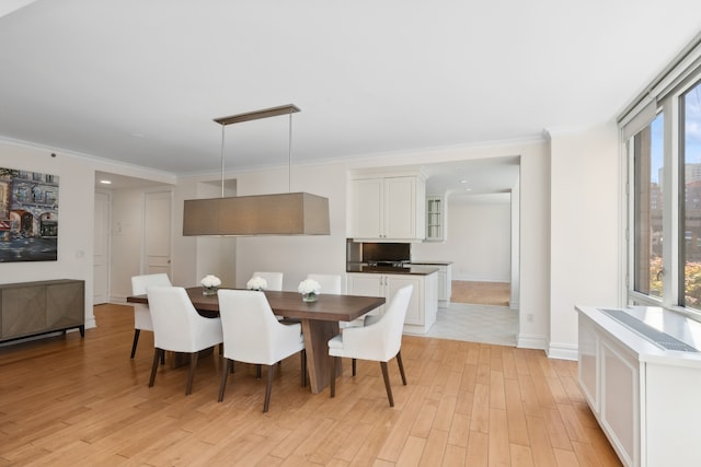 dining area with light wood-style floors, ornamental molding, and baseboards