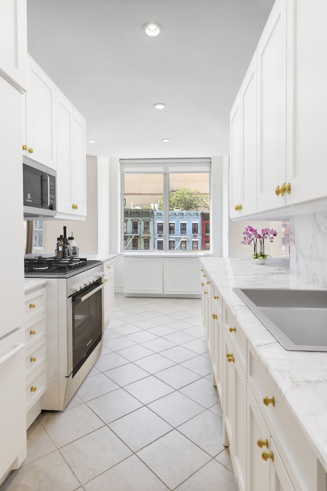 kitchen featuring light tile patterned floors, appliances with stainless steel finishes, white cabinetry, and light stone countertops