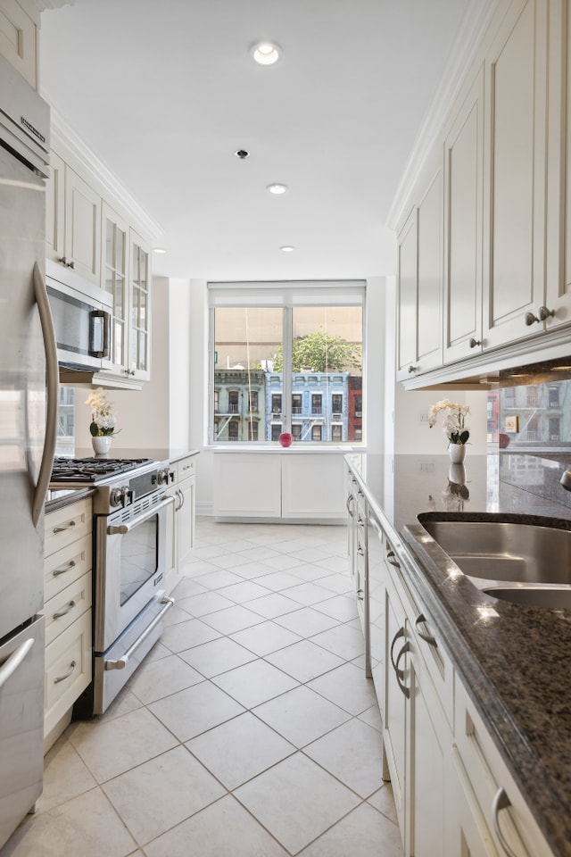 kitchen with light tile patterned flooring, stainless steel appliances, a sink, white cabinets, and dark stone countertops