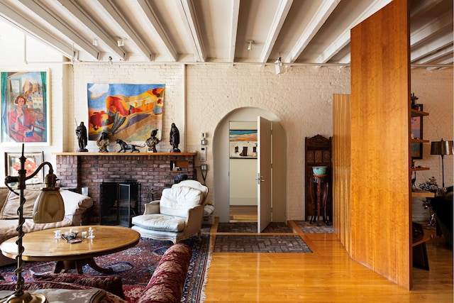 living room with beam ceiling, a brick fireplace, arched walkways, and wood finished floors