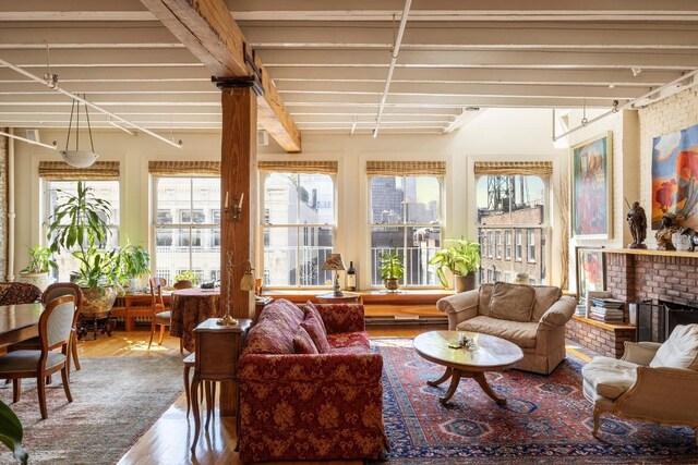 living room with a brick fireplace, brick wall, hardwood / wood-style flooring, and beamed ceiling