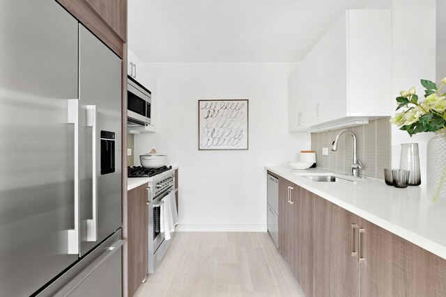 kitchen with white cabinetry, sink, decorative backsplash, built in appliances, and light hardwood / wood-style flooring