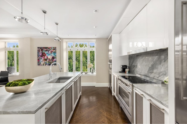 kitchen with appliances with stainless steel finishes, a sink, light stone countertops, baseboards, and white cabinetry