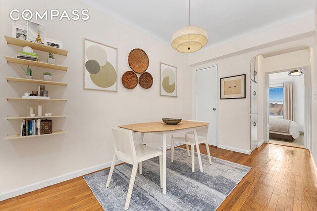 dining room featuring wood-type flooring, arched walkways, and baseboards