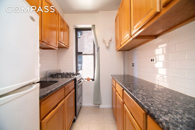 98 Park Ter E Unit 3A, New York City, NY 10034 - kitchen with freestanding refrigerator, decorative backsplash, gas range, light tile patterned floors, and dark stone counters
