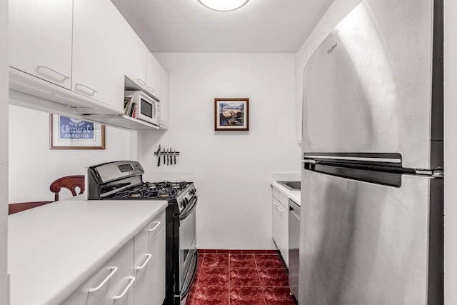 kitchen with light countertops, appliances with stainless steel finishes, dark tile patterned flooring, and white cabinetry