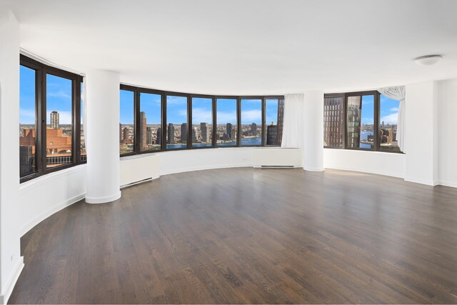 unfurnished room featuring a view of city, wood finished floors, and baseboards