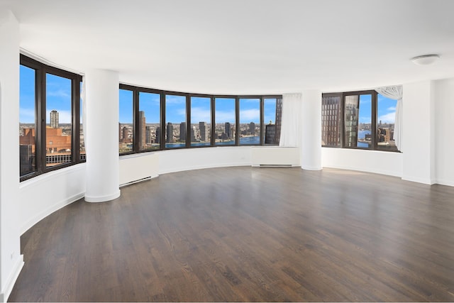 unfurnished room with a view of city, wood finished floors, and baseboards