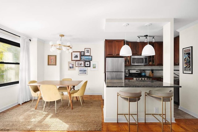 kitchen featuring stainless steel appliances, dark stone countertops, backsplash, hanging light fixtures, and a breakfast bar