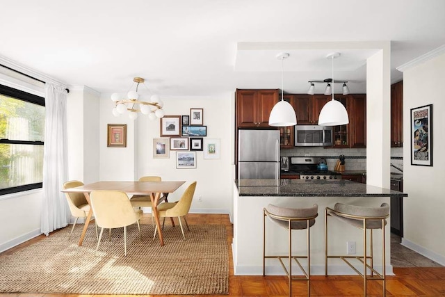 kitchen featuring a notable chandelier, appliances with stainless steel finishes, hanging light fixtures, a kitchen breakfast bar, and decorative backsplash