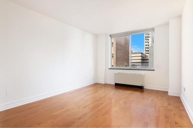 spare room featuring light wood-type flooring, radiator, and baseboards