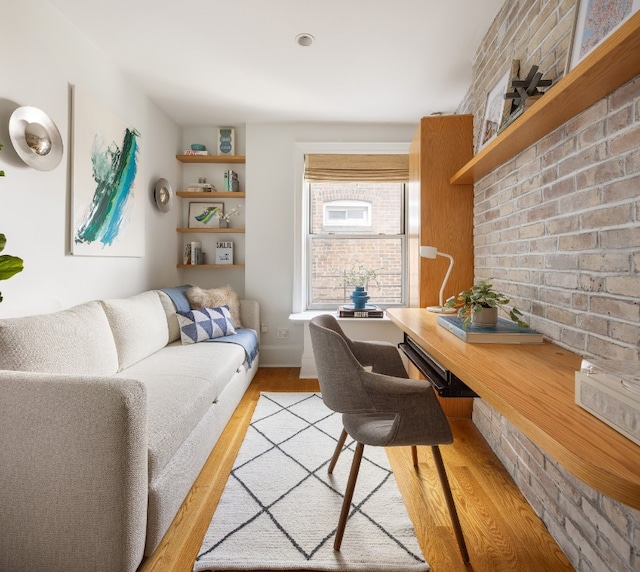 office space featuring brick wall, light wood-style flooring, and baseboards