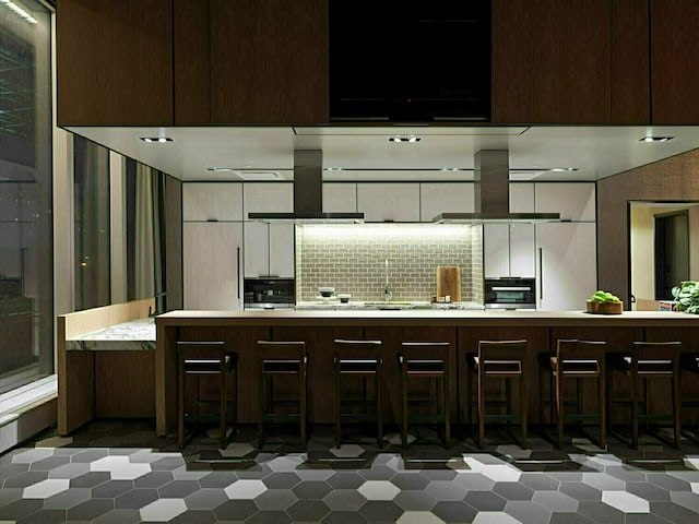 252 S St Unit 76E, New York City, NY 10002 - kitchen with wall chimney exhaust hood, stainless steel oven, island range hood, tasteful backsplash, and light countertops