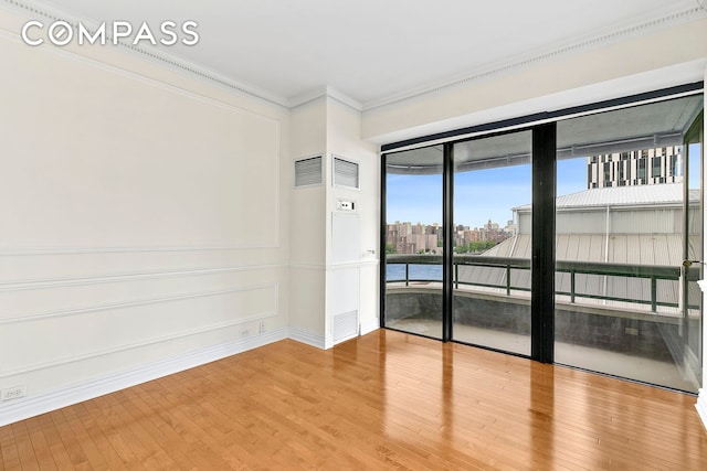 spare room with a view of city, wood finished floors, visible vents, and ornamental molding