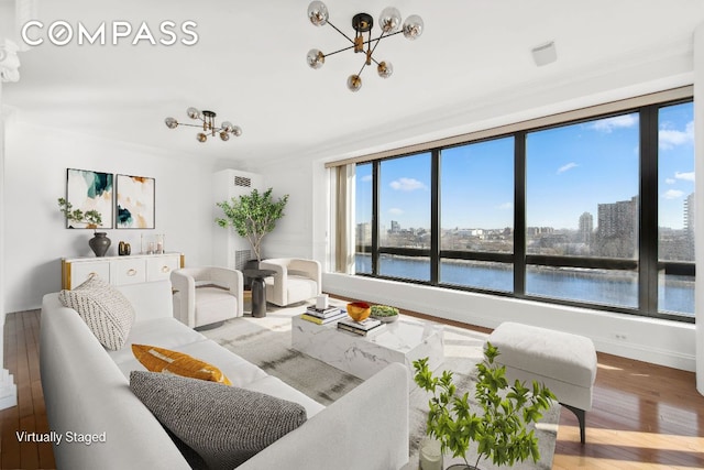 living room with a chandelier, a water view, wood finished floors, baseboards, and crown molding