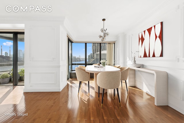 dining area with an inviting chandelier, ornamental molding, wood-type flooring, a city view, and a decorative wall