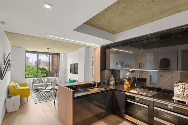 kitchen with sink, appliances with stainless steel finishes, decorative backsplash, decorative light fixtures, and light wood-type flooring