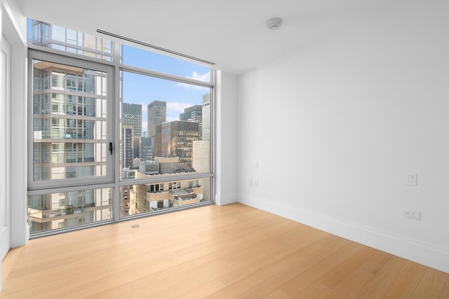 unfurnished room with wood finished floors, floor to ceiling windows, plenty of natural light, a view of skyline, and baseboards
