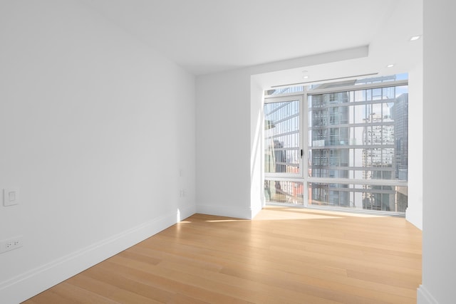 empty room featuring wood finished floors, baseboards, floor to ceiling windows, and a city view