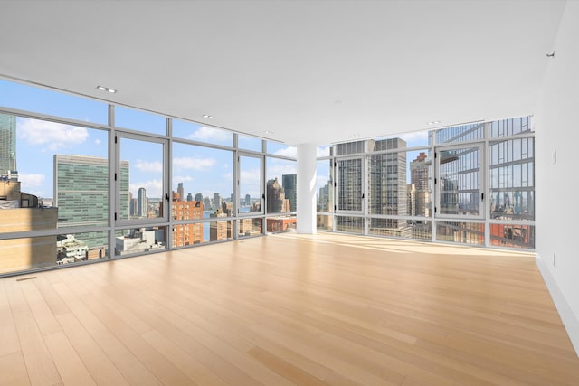 empty room featuring a view of skyline, wood finished floors, a wall of windows, and healthy amount of natural light