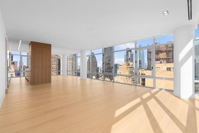 empty room with a view of skyline, light wood-type flooring, and expansive windows