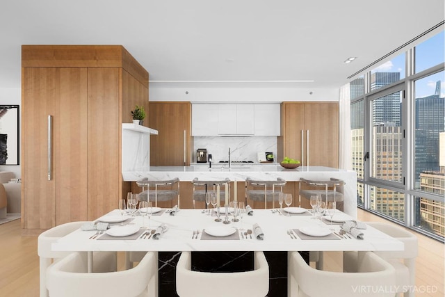 kitchen featuring sink, backsplash, white cabinetry, a wall of windows, and light hardwood / wood-style floors