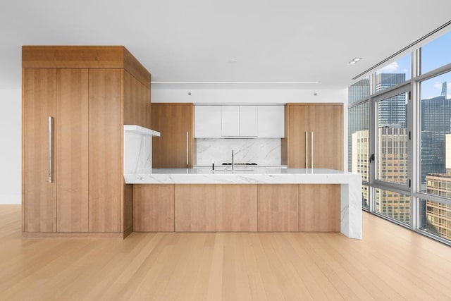 kitchen featuring tasteful backsplash, white cabinets, light hardwood / wood-style floors, expansive windows, and kitchen peninsula