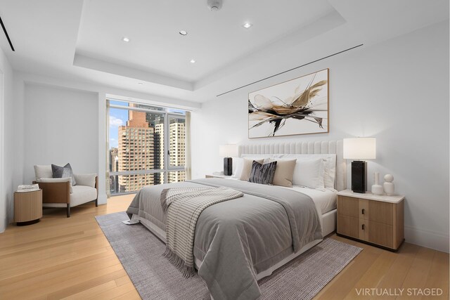 bedroom featuring light wood-type flooring and a raised ceiling