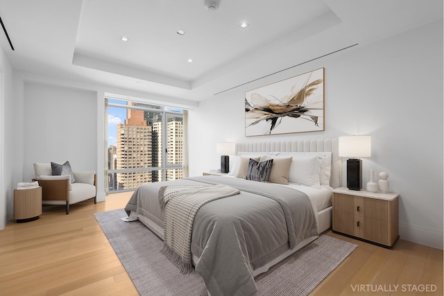 bedroom with a tray ceiling, light wood finished floors, recessed lighting, a view of city, and baseboards