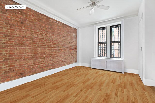 empty room with baseboards, brick wall, radiator heating unit, ceiling fan, and wood finished floors