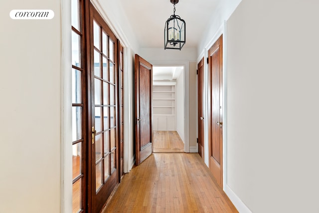 hall featuring built in shelves, baseboards, a chandelier, light wood-style flooring, and french doors