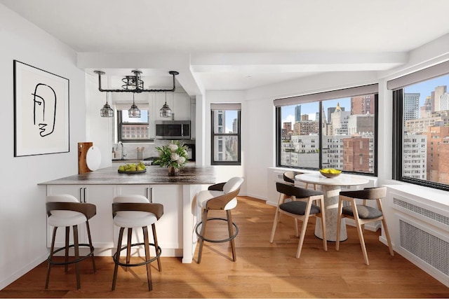 interior space with pendant lighting, radiator, a breakfast bar, light hardwood / wood-style floors, and kitchen peninsula