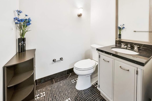 half bathroom with tile patterned flooring, baseboards, vanity, and toilet