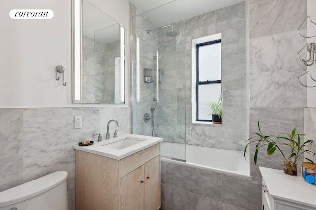 full bath with tile walls, vanity, toilet, and tiled shower / bath combo