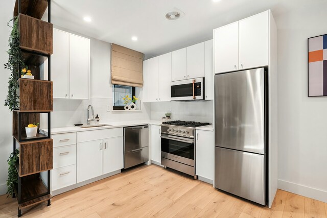 kitchen with stainless steel appliances, white cabinetry, sink, and light hardwood / wood-style flooring