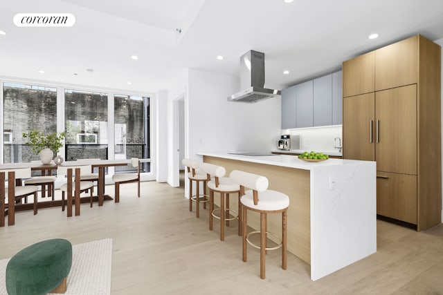 kitchen with black electric stovetop, ventilation hood, a breakfast bar area, and light wood-type flooring