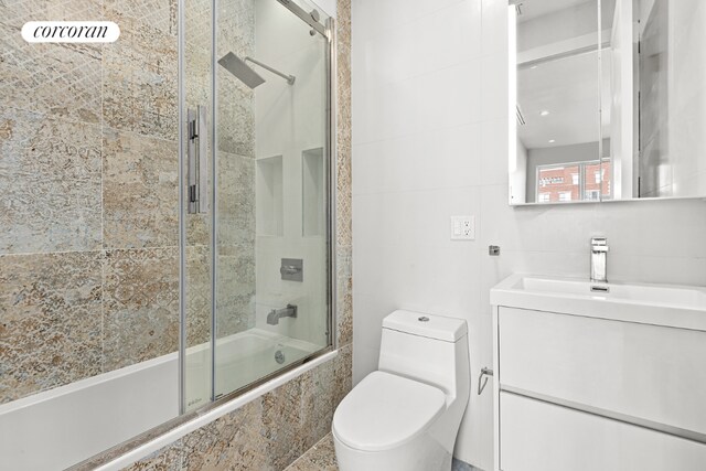 full bathroom with combined bath / shower with glass door, vanity, and toilet