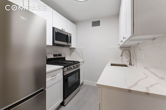 kitchen featuring stainless steel appliances, backsplash, white cabinetry, a sink, and light stone countertops