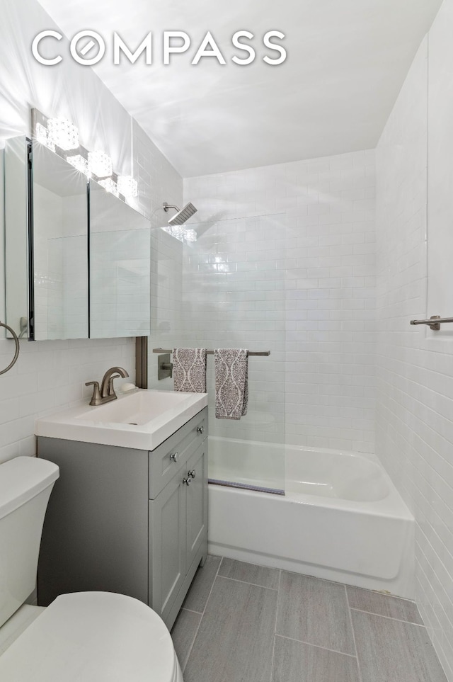 bathroom featuring toilet,  shower combination, tile walls, and vanity