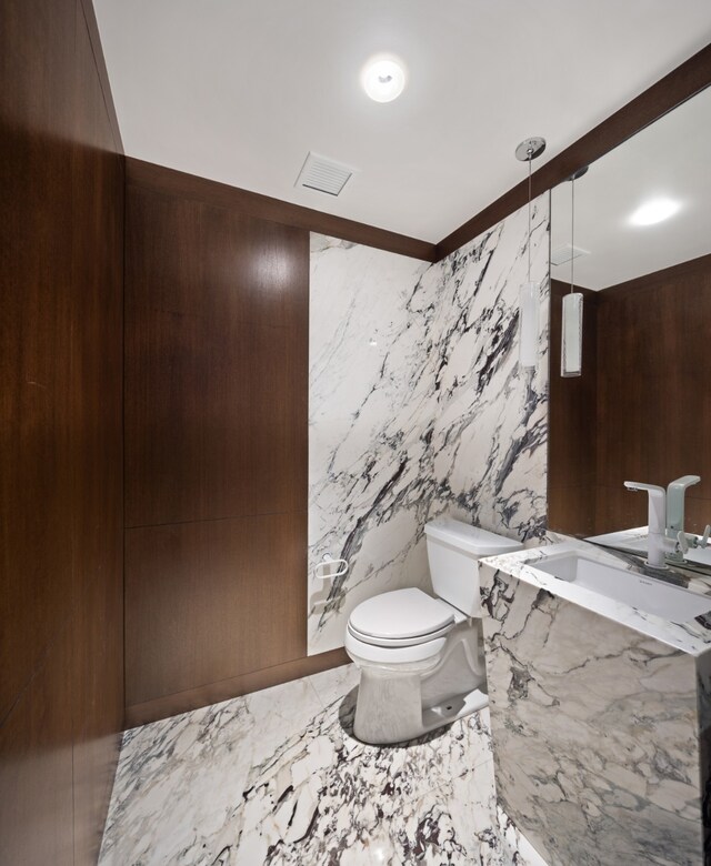 bathroom featuring marble finish floor, visible vents, toilet, a sink, and stone wall