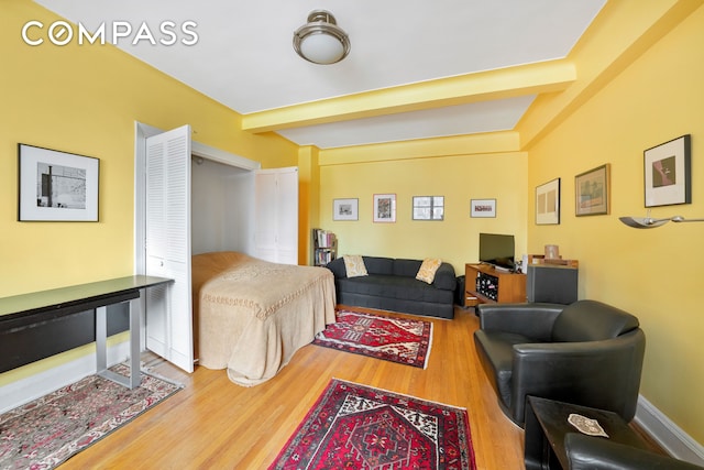 living area featuring baseboards, beam ceiling, and wood finished floors