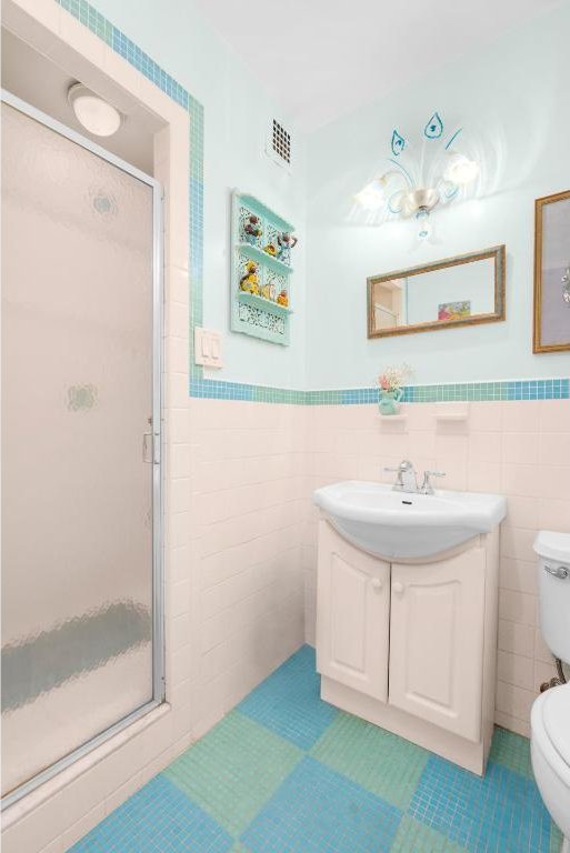 bathroom featuring toilet, vanity, tile walls, tile patterned floors, and a shower with shower door