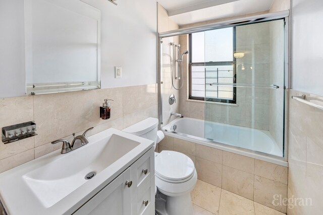 full bathroom with toilet, bath / shower combo with glass door, tile walls, and vanity