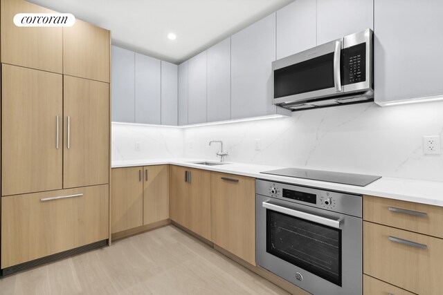 kitchen featuring backsplash, sink, light wood-type flooring, appliances with stainless steel finishes, and white cabinets