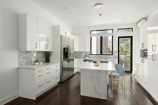 kitchen with stainless steel refrigerator with ice dispenser, a kitchen bar, white cabinetry, a center island, and dark hardwood / wood-style floors