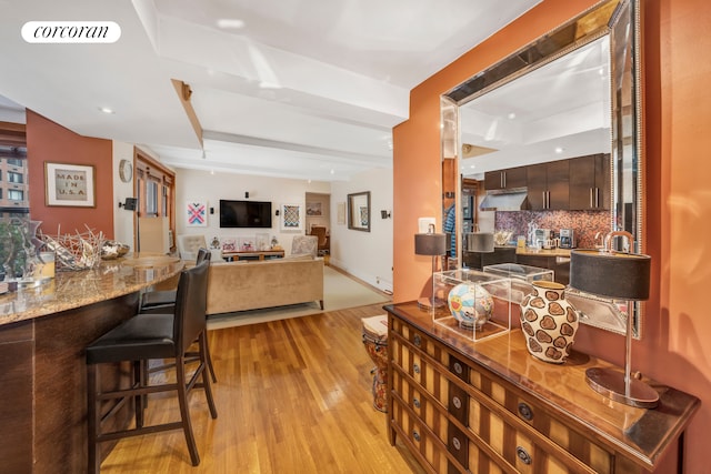 kitchen featuring a breakfast bar area, visible vents, decorative backsplash, light wood-type flooring, and beamed ceiling